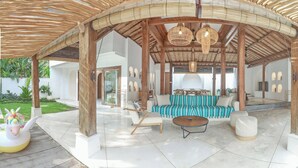 A covered outdoor seating area with a wooden structure, a sofa, a round table, and a decorative unicorn float. - Central Canggu Walk to Nelayan Beach - 3BR Villa (kuta utara)