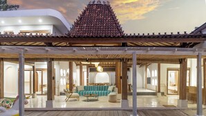A traditional-style building with a tiled roof and wooden beams, featuring a spacious interior with a sofa and chairs, and a view of the surrounding area. - Central Canggu Walk to Nelayan Beach - 3BR Villa (kuta utara)