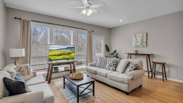 A living room with a sofa, coffee table, TV, and large windows with blinds.