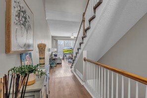 Una escalera con barandillas blancas y baranda de madera, que conduce a una habitación con vistas al exterior.