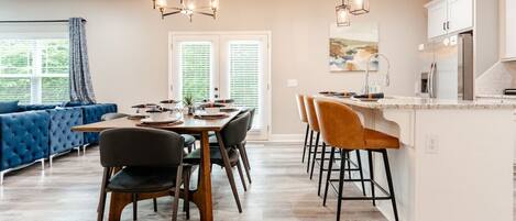 A modern kitchen with a dining area, featuring a large island with bar stools, a blue sofa, and a chandelier.