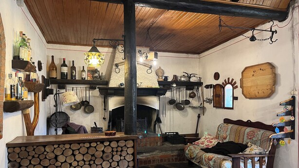 Ein rustikaler Innenraum mit Kamin aus Stein, Holzregalen mit Flaschen und einer gemütlichen Sitzecke.