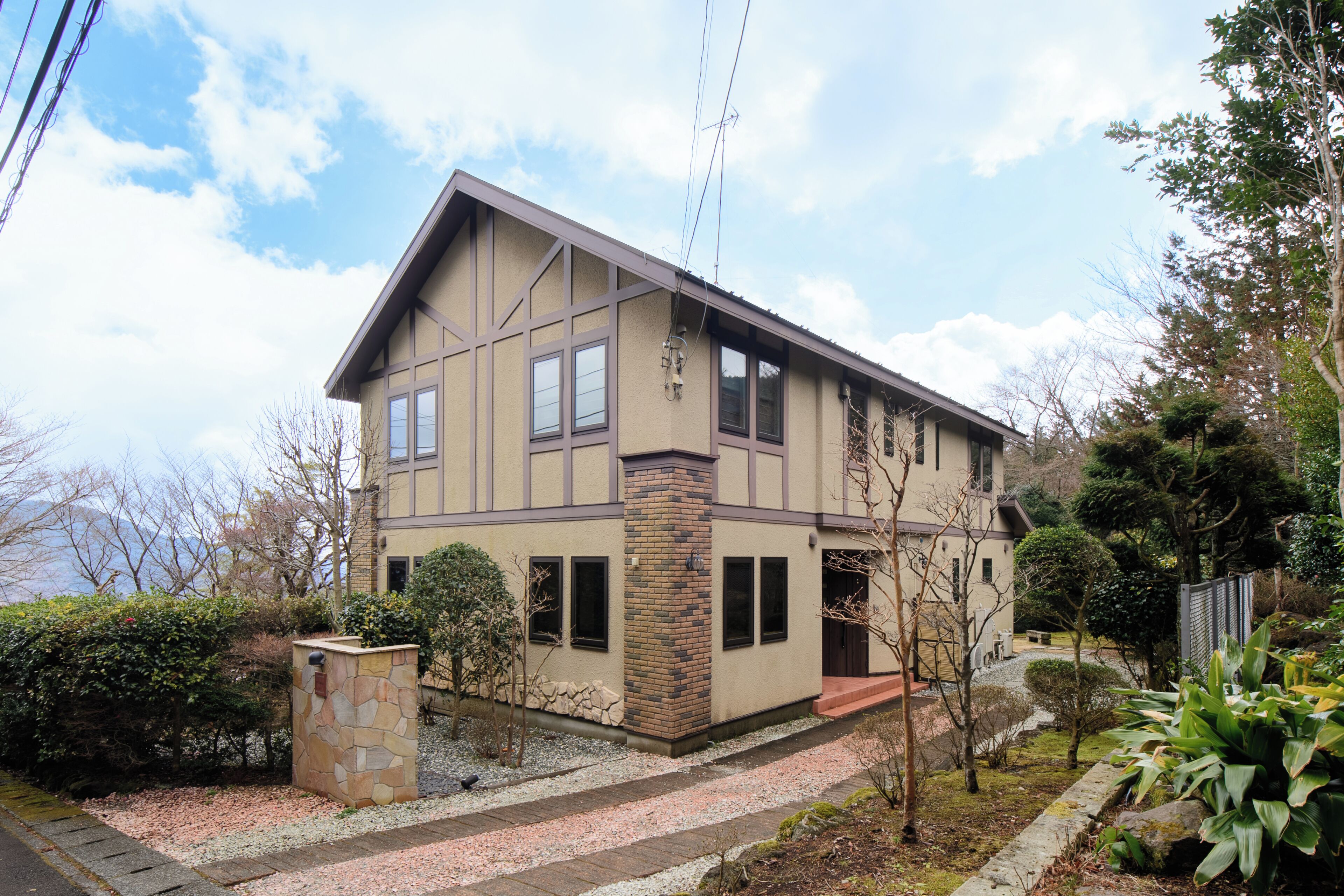 A two-story house with a stone pillar, a small garden, and a view of the sky.