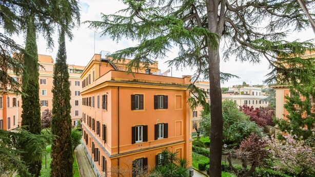 A multi-story building with a symmetrical facade, surrounded by lush greenery and other buildings. - Villa Riccio-Flaminio House (Roma)