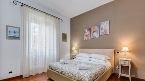 A neatly arranged bedroom with a large bed, two bedside tables with lamps, a curtain, and wall art. - Villa Riccio-Flaminio House (Roma)