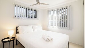 A hotel room with a bed, a nightstand with a lamp, a ceiling fan, and windows with blinds. - Smart Suites Self Check-in Apartments - 19 Darnley (Rocklea)