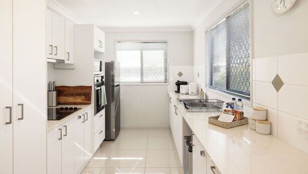 A modern kitchen with white cabinetry, stainless steel appliances, and a window with blinds. - Smart Suites Self Check-in Apartments - 19 Darnley (Rocklea)