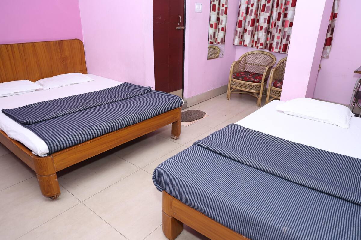 Dos camas de madera con ropa de cama a rayas en una habitación con paredes rosadas, una silla de mimbre y una puerta.