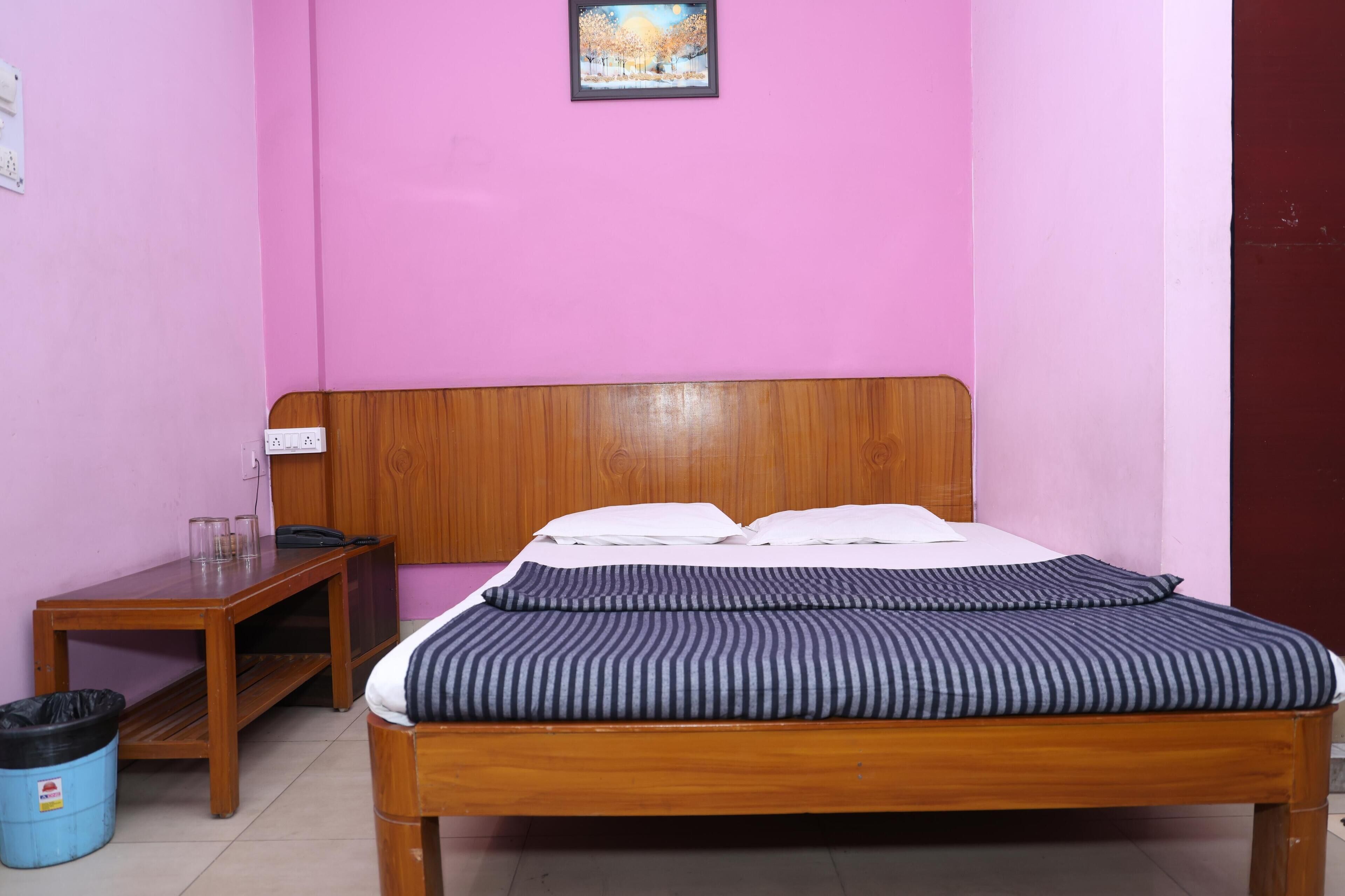 Un dormitorio con una cama de madera, paredes rosadas, una mesita de madera y un cubo de basura azul.
