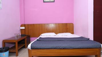 Een slaapkamer met een houten bed, roze wanden, een klein houten tafeltje en een blauwe prullenbak.