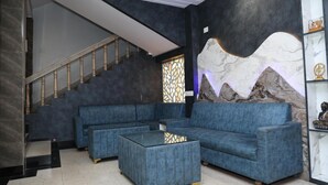 A modern living room with a blue sofa set, a glass coffee table, and a staircase with wooden railings. - Hotel Hill View (Jamshedpur)