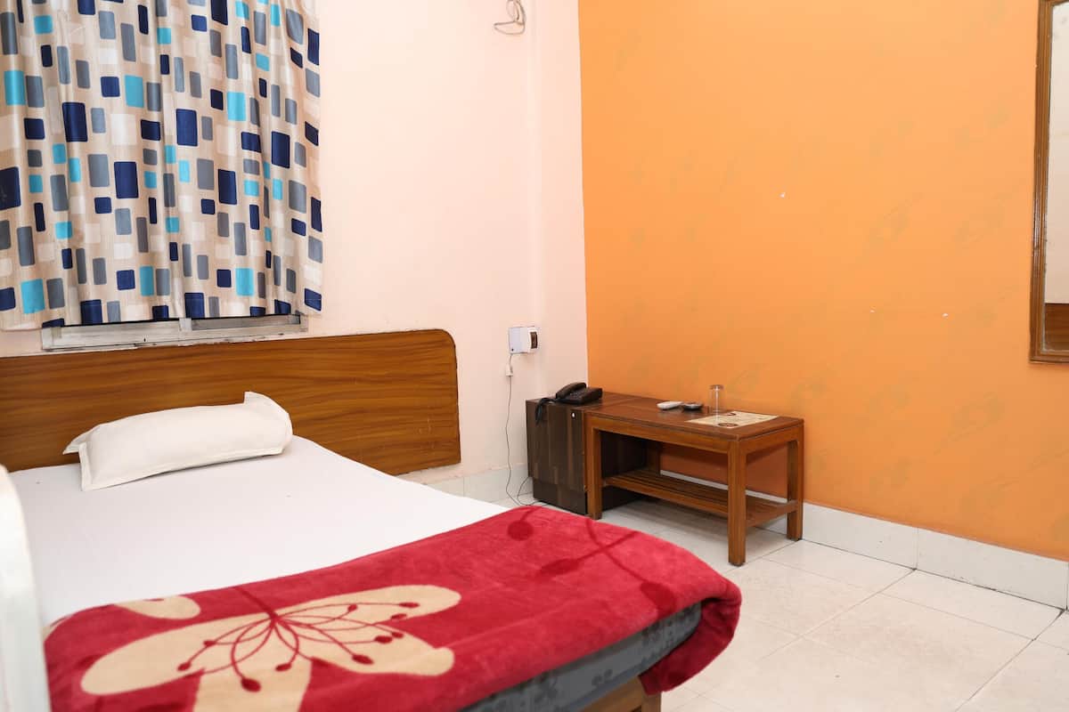 Una habitación de hotel con cama, mesita de noche de madera, teléfono y ventana con cortinas.