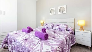 A bedroom with a bed, two wall art pieces, a nightstand with a lamp, and rolled towels on the bed. - Apartment With air Conditioning, Parking and Wi-fi (Denia)