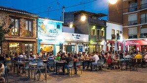 An outdoor café with tables and chairs, surrounded by buildings with various signs and storefronts. - Apartment With air Conditioning, Parking and Wi-fi (Denia)