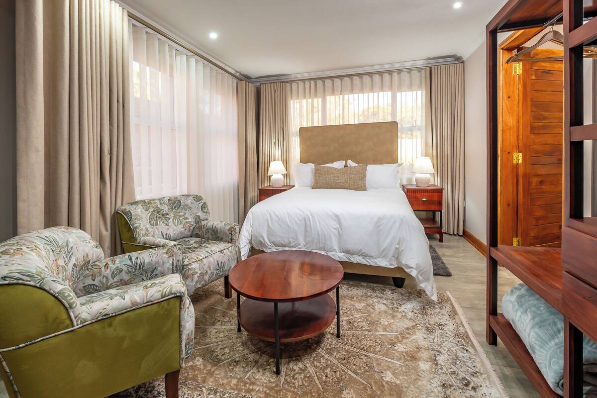 A hotel room with a bed, a round wooden table, a floral armchair, and a wardrobe.