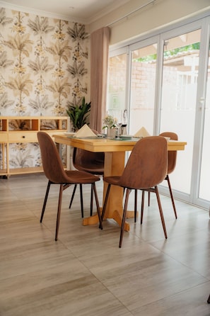 A dining area with a wooden table and brown chairs, a bookshelf, and a large window with a view. - 36 Alexander Guest House  (Harare)