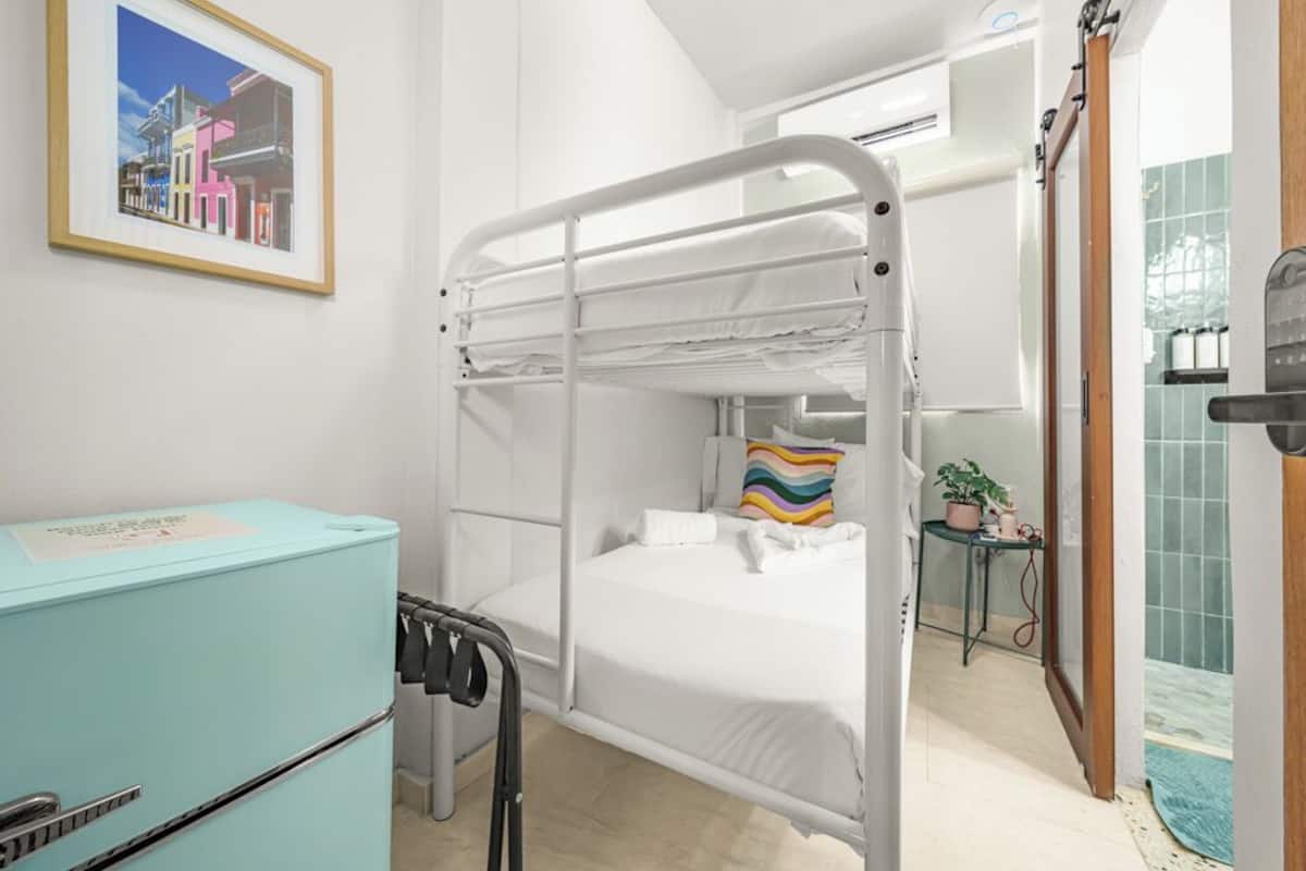 Dormitorio con literas, un aparador azul claro, un cuadro en la pared y una pequeña mesa con una planta.