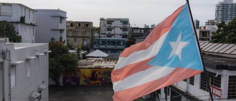 A flag on a pole in an urban setting with buildings and a mural in the background.