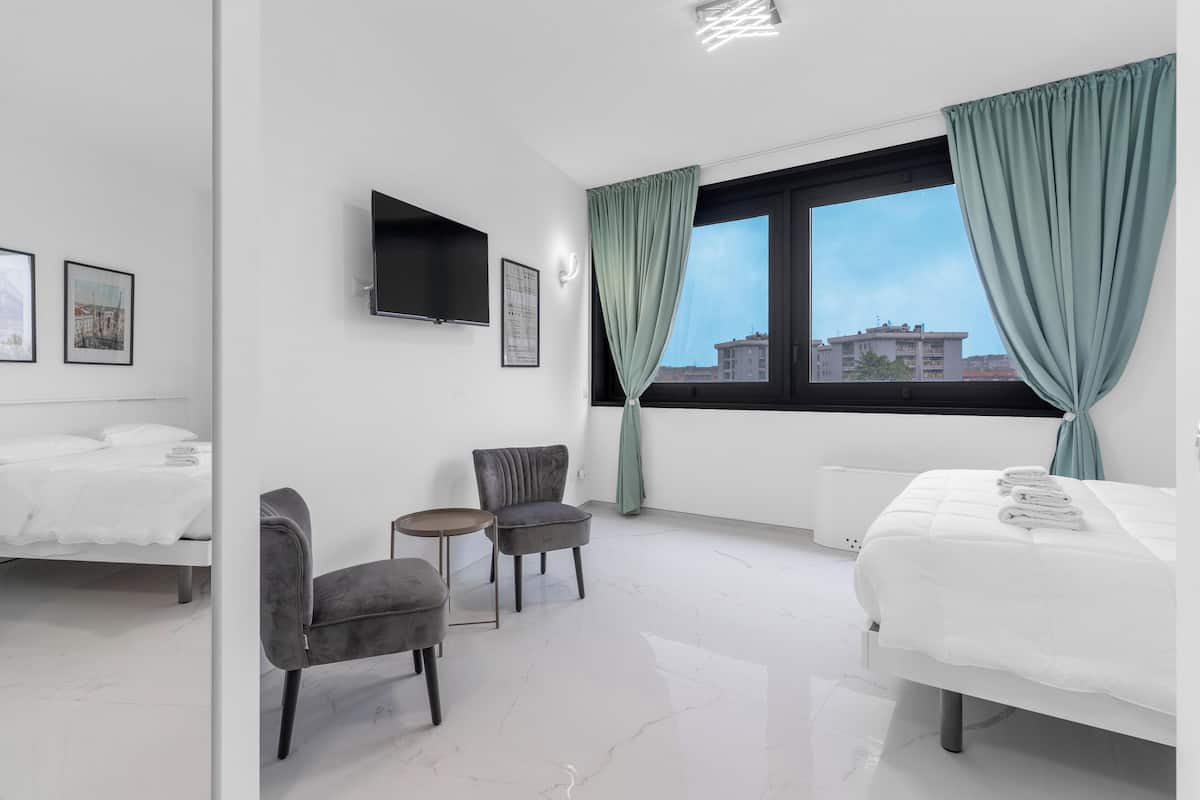 Ein modernes Hotelzimmer mit Bett, zwei Stühlen, einem kleinen Tisch, einem Fernseher und einem fenster mit Vorhängen.