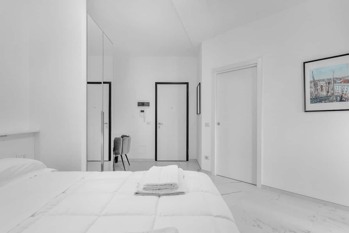 Ein modernes Hotelzimmer mit einem großen Bett, einem Sessel, einer Tür und einem gerahmten Bild an der Wand.