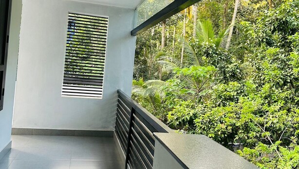 Un balcón con vistas a abundante vegetación, una ventana con persianas horizontales y una lámpara de techo.