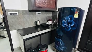 Une cuisine compacte équipée d’un micro-ondes encastré, d’un petit plan de travail, d’un réfrigérateur orné de motifs floraux et de deux poubelles.