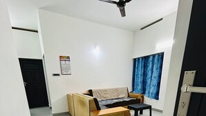 Una habitación con sofá, una mesita, ventilador de techo, ventana con cortinas azules y una puerta.