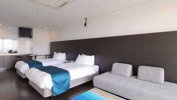 A modern hotel room with two beds, a sofa, a kitchen area, and a flat-screen TV.