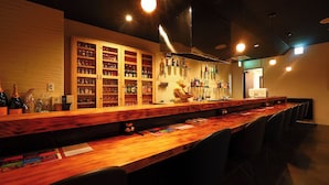 Un espace bar avec des étagères en bois remplies de bouteilles et de verres, une sculpture d’ours et un long comptoir en bois.