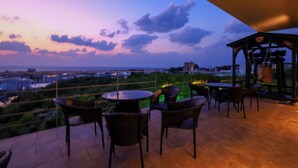 Une terrasse avec des sièges extérieurs et une vue sur les toits de la ville au crépuscule.