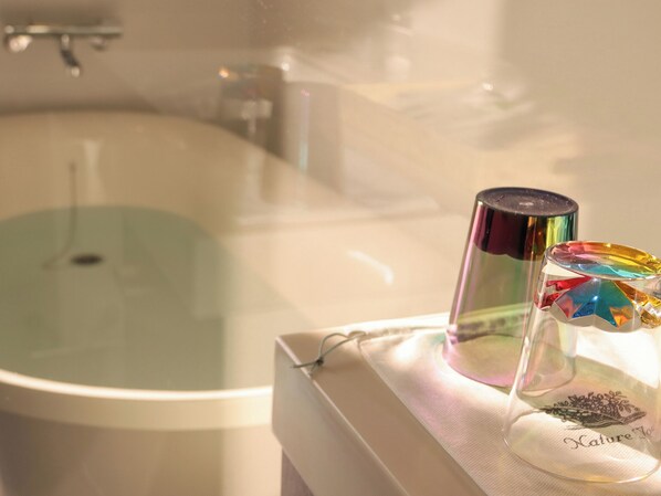 Un baño con una bañera, un recipiente de vidrio y una botella sobre una toalla.