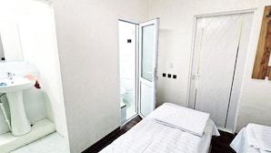 A small, compact room with a white sink, a mirror, a door, and a bed with a white cover. - Best hotel (Tashkent)