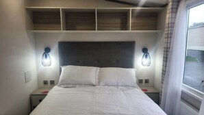 A bedroom with a bed, bedside lamps, a headboard, and a window with curtains. - Luxury caravan, Newquay Bay. Amazing views. (Newquay )