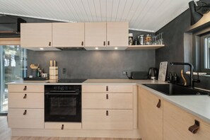 Una cocina moderna con armarios de madera clara, un lavavajillas negro y un ventanal grande.