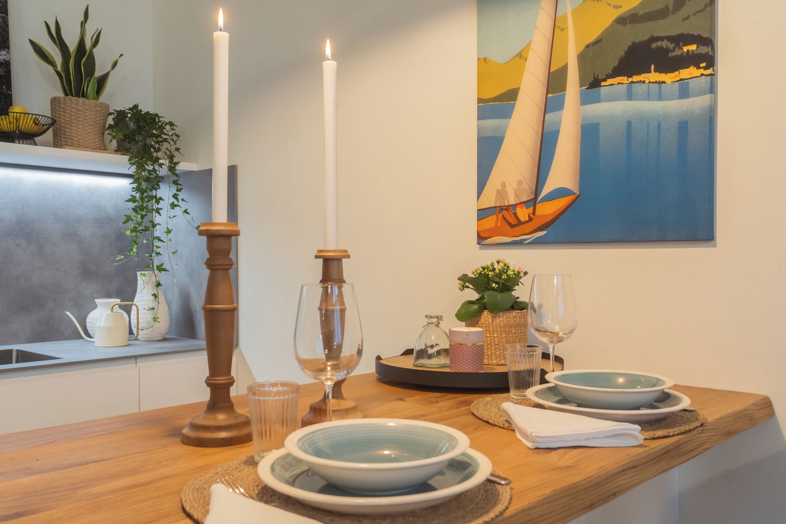 A wooden dining table with white plates, a candle, and a painting of a sailboat.
