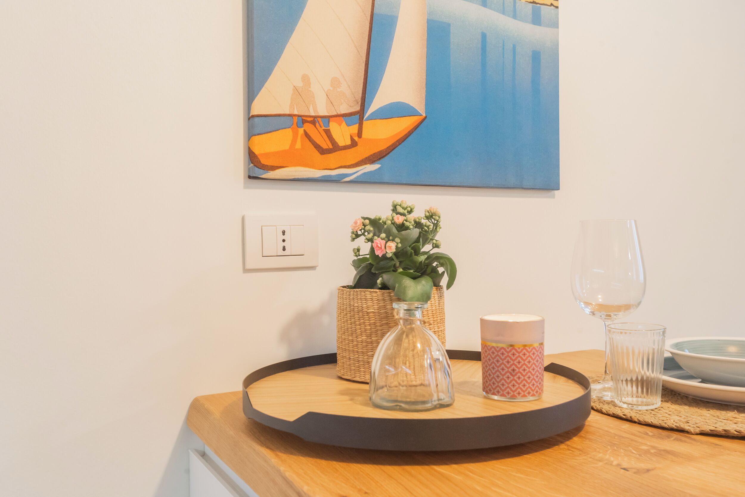 Un plateau en bois avec une bouteille en verre, une plante en pot, une tasse à motifs et un verre, le tout posé sur une table.