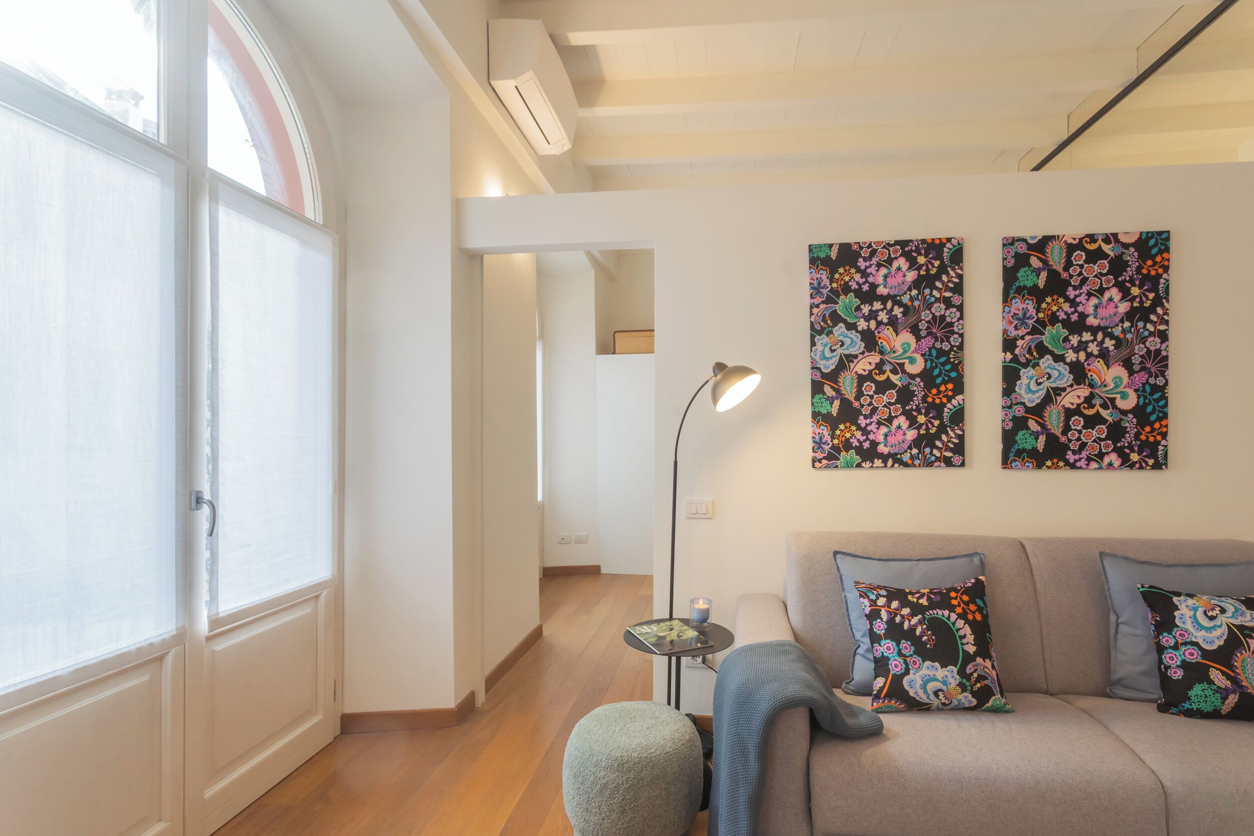 Un salon comprenant un canapé, deux coussins à motifs, une lampe sur pied et une petite table sur laquelle est posée une bougie.