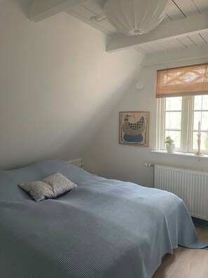 Une chambre à coucher avec un lit, un radiateur, une fenêtre avec des rideaux et un élément décoratif mural.