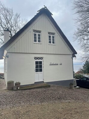 A two-story house with a white exterior, a gabled roof, and a front door.