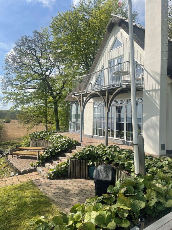 A house with a balcony, large windows, and a garden with plants and a bench.