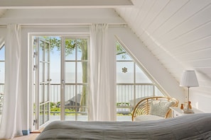 A bedroom with a large window, a bed, a chair, and a lamp.