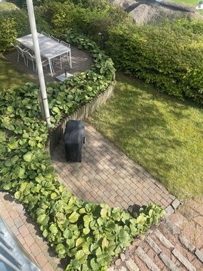 Un espace extérieur aménagé avec une terrasse dallée, une table et des chaises, entouré d’une végétation luxuriante et d’une pelouse.