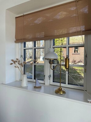 A window with a view of a brick building, a white vase with dried plants, and a brass floor lamp.
