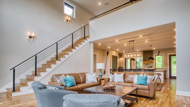 A spacious living room with a staircase, wooden flooring, and a kitchen area visible in the background. - Family House on Watauga River (Johnson City)