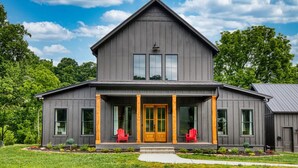A two-story house with a dark gray exterior, a prominent front porch with red chairs, and a large front door. - Family House on Watauga River (Johnson City)