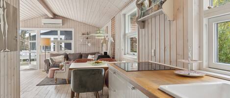 A modern kitchen with wooden cabinets, a dining area with a table and chairs, and a large window providing natural light.