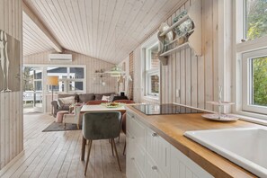 A modern kitchen with wooden cabinets, a dining area with a table and chairs, and a large window providing natural light.