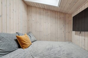 A bedroom with a bed, a skylight, and wooden walls.