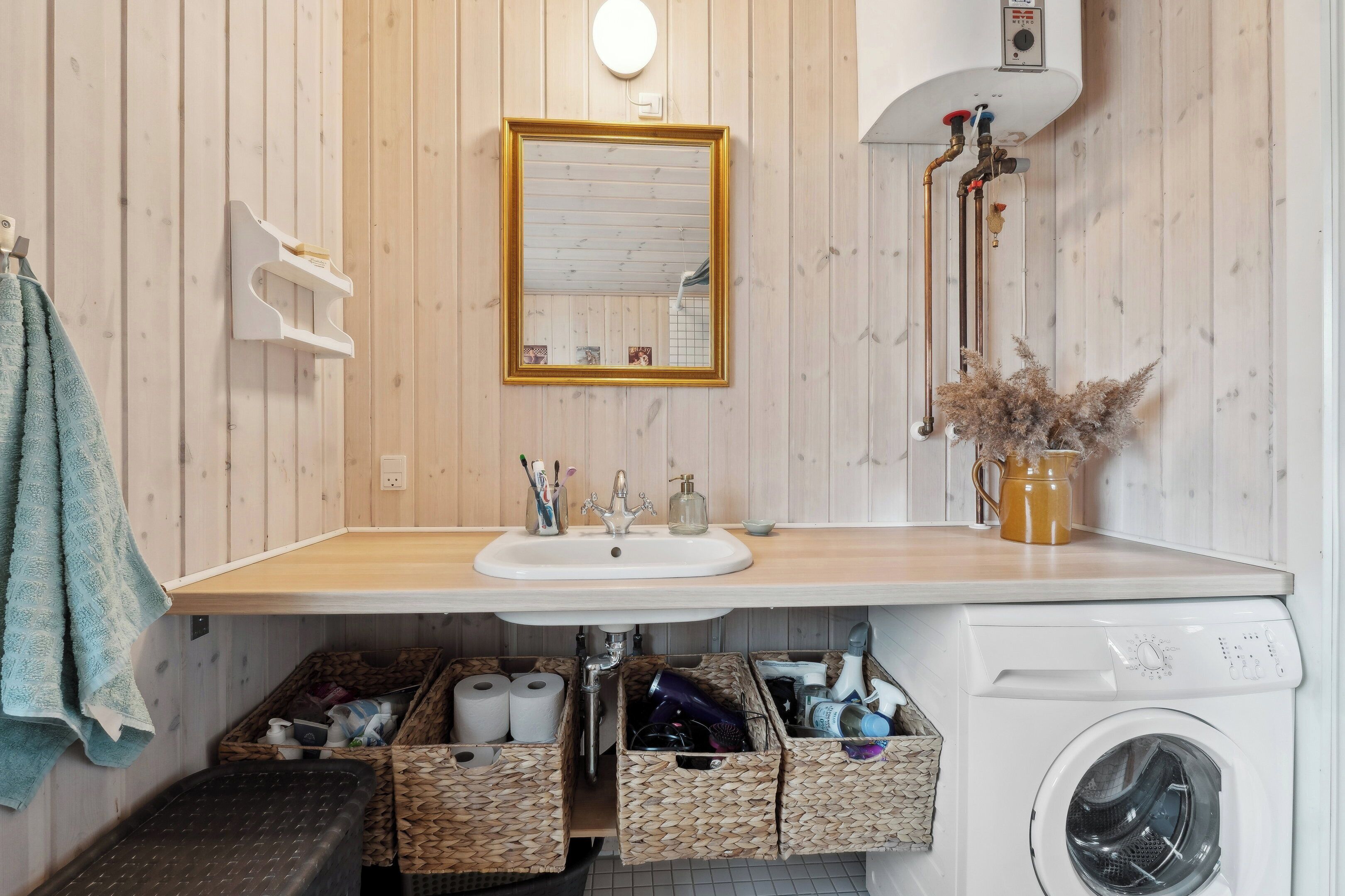 Un baño con tocador de madera, lavamanos, espejo, lavadora y cestas de almacenamiento.