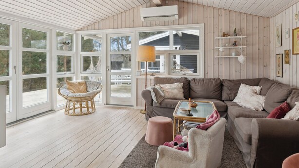 En hyggelig stue med en brun sofa, en fletstol og et sofabord i glas.